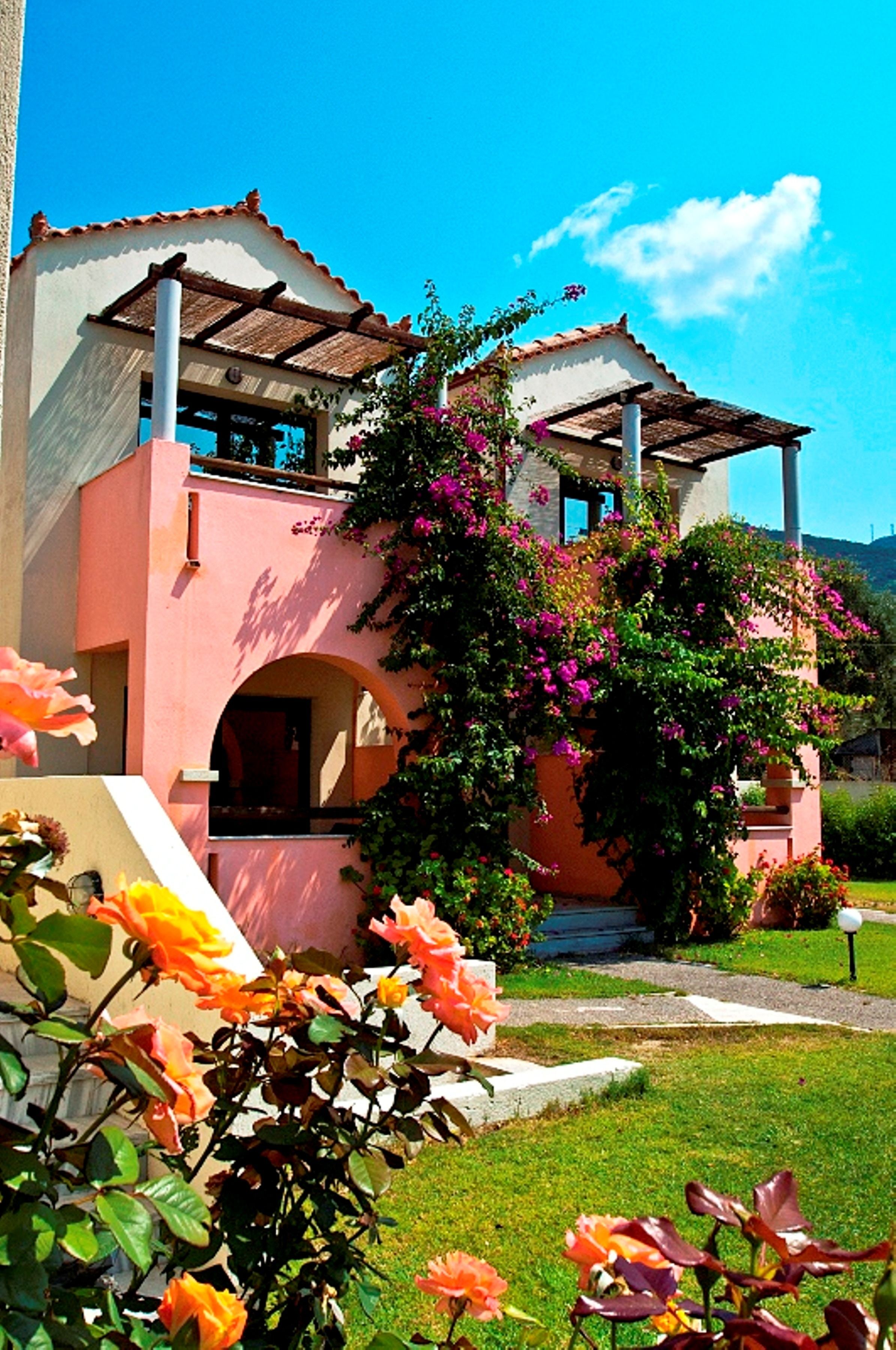 A two-story building with a pink facade, a balcony, and a garden with orange flowers.
