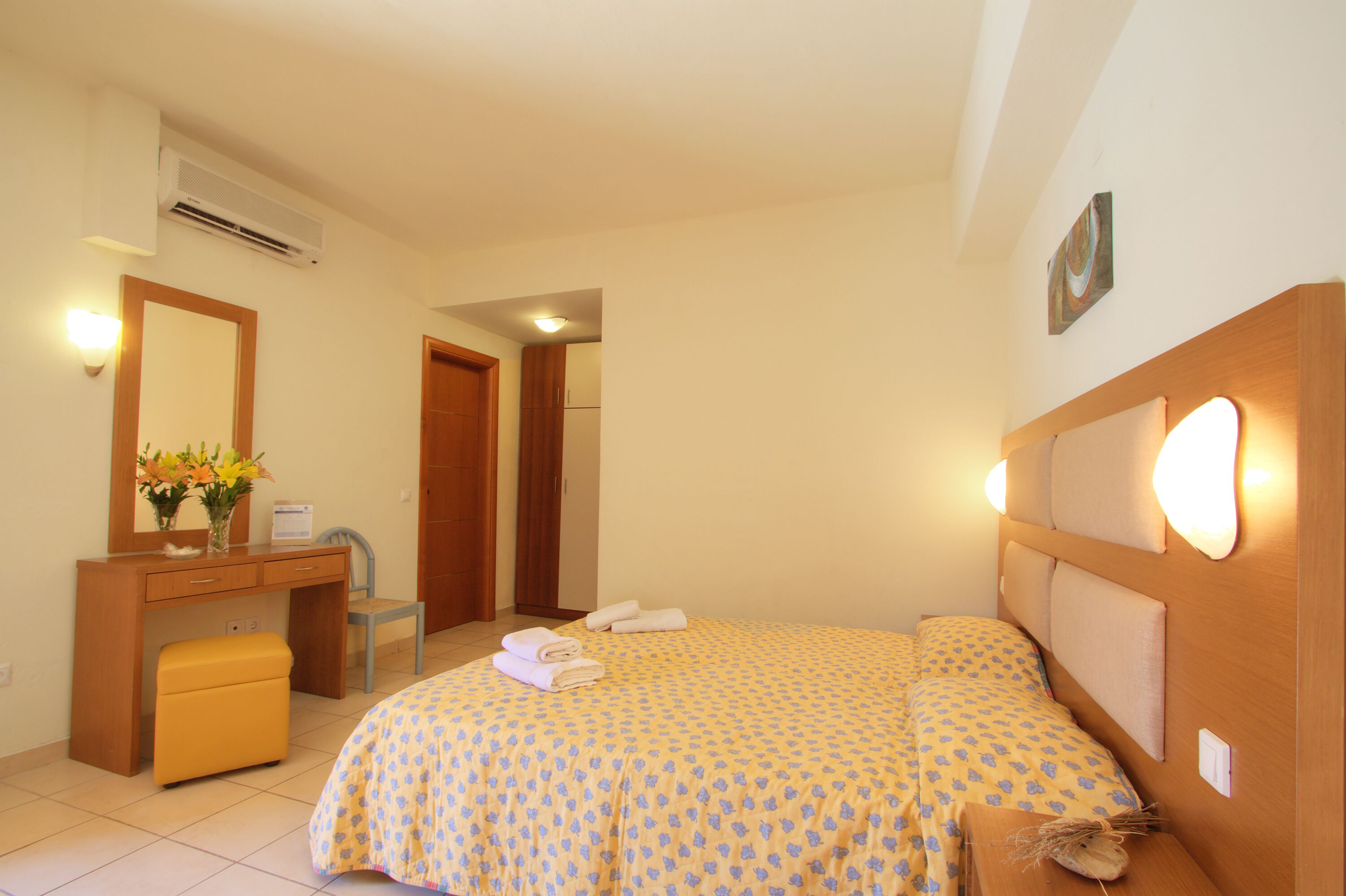 A bedroom with a bed, a desk, a chair, and a small table with towels.