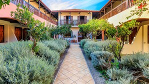 A courtyard with a tiled pathway, surrounded by neatly trimmed shrubs and potted plants. - Rigas Hotel Skopelos by GHH (Skopelos)
