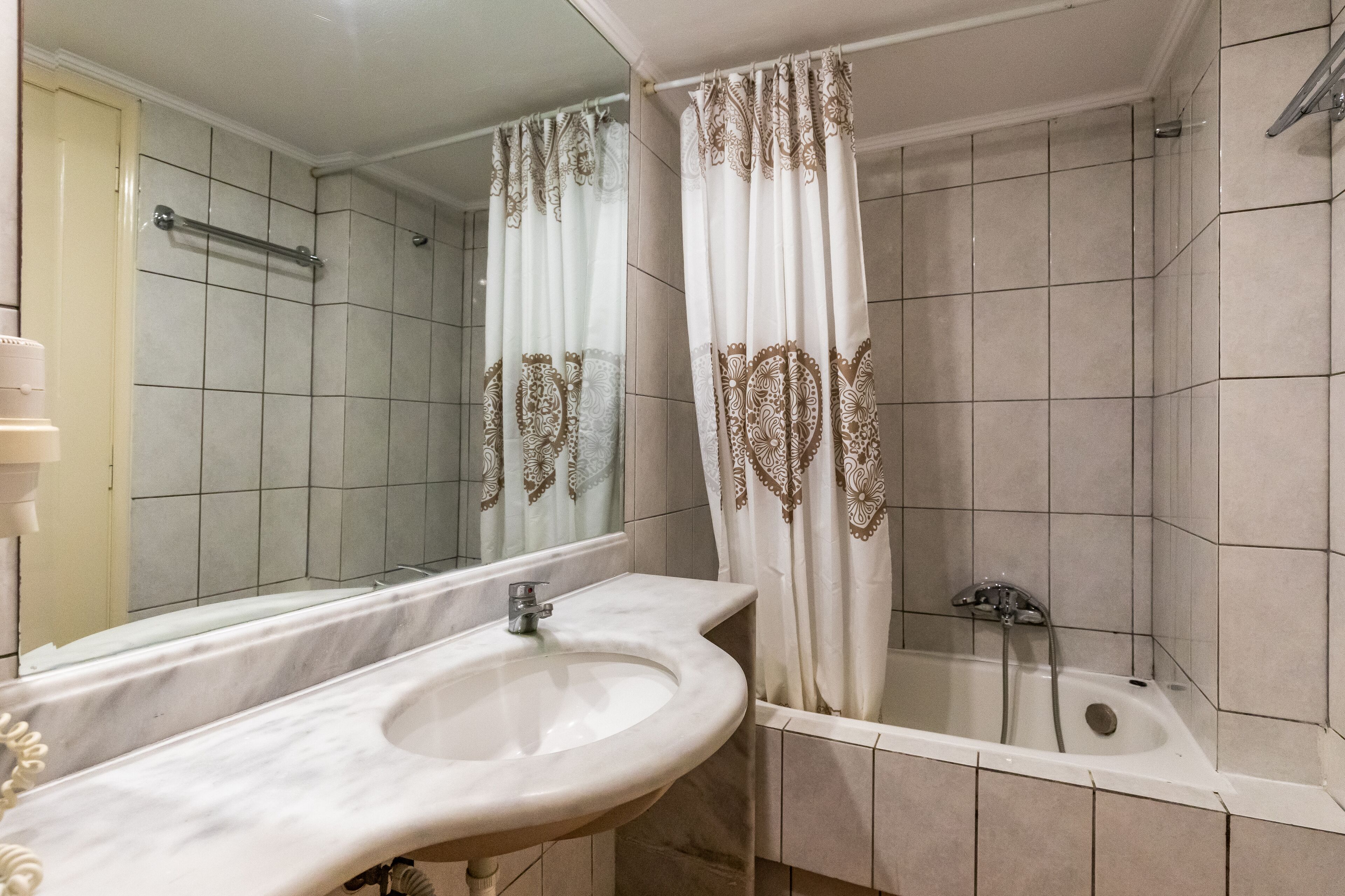 A bathroom with a sink, mirror, bathtub, and shower curtain.