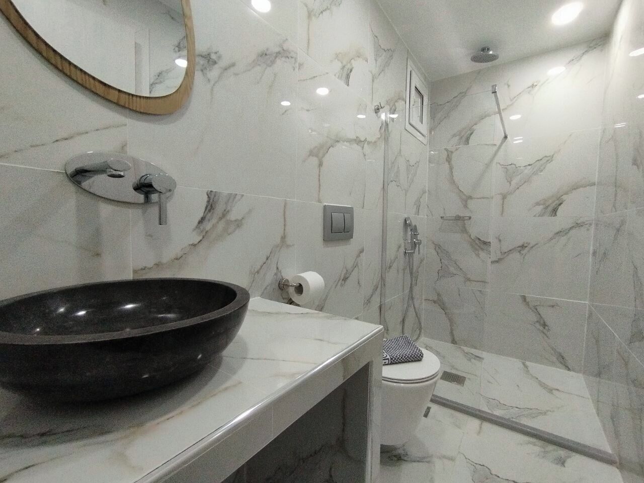A bathroom with a marble sink, a mirror, a shower, and a toilet.