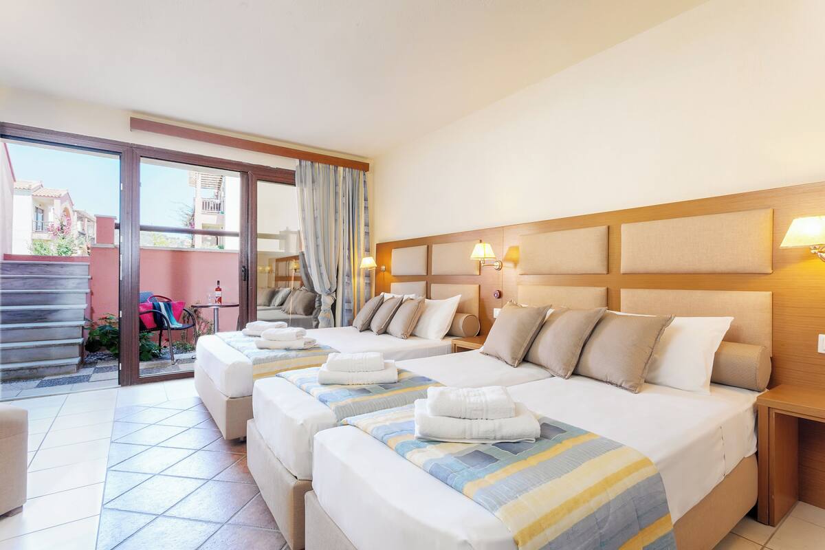 A hotel room with two beds, a balcony, and a view of the outside.