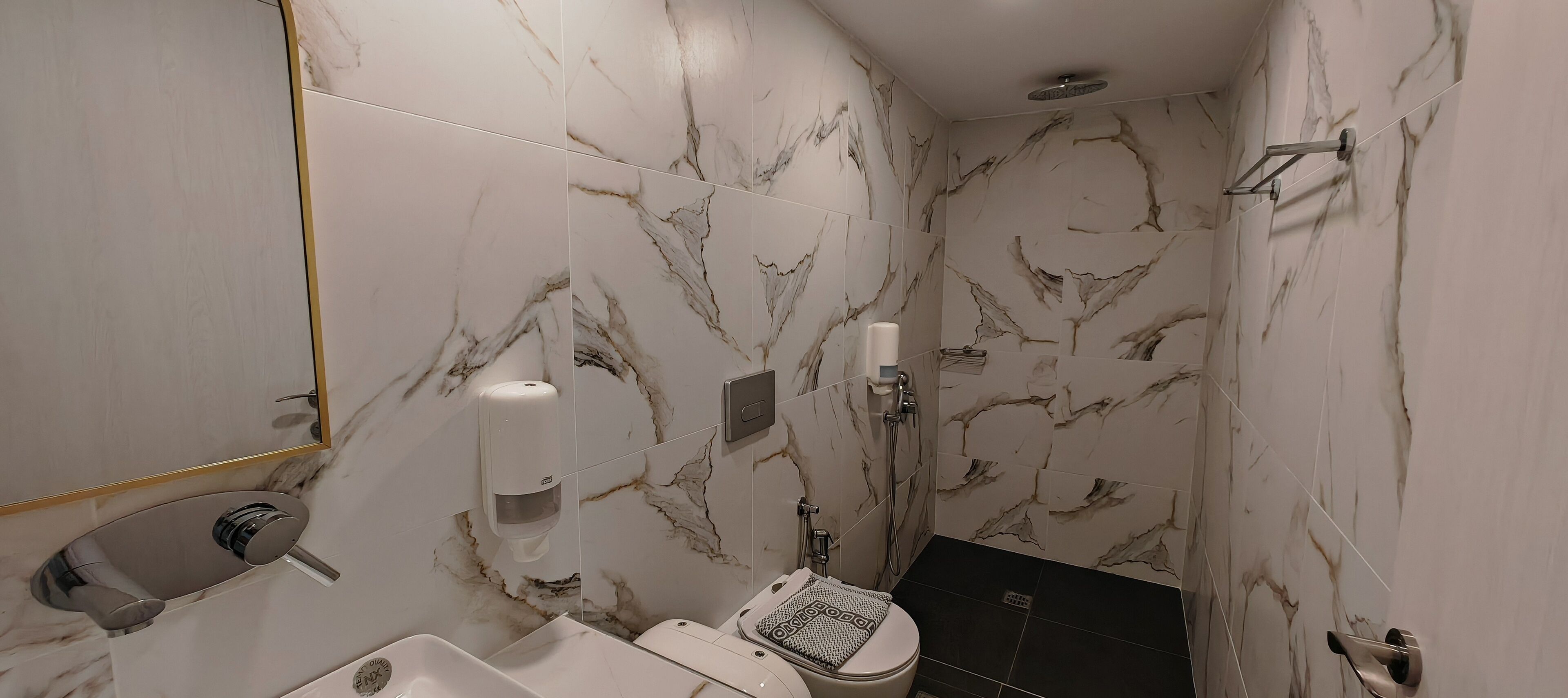 A bathroom with marble walls, a toilet, a sink, and a shower.