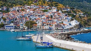 A coastal town with white buildings and red roofs, a marina with boats, and a rocky shoreline. - Rigas Hotel Skopelos by GHH (Skopelos)