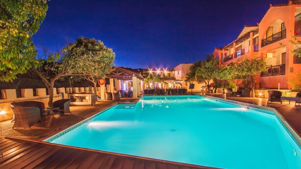 A swimming pool with a wooden deck, surrounded by outdoor seating and a building with balconies.
