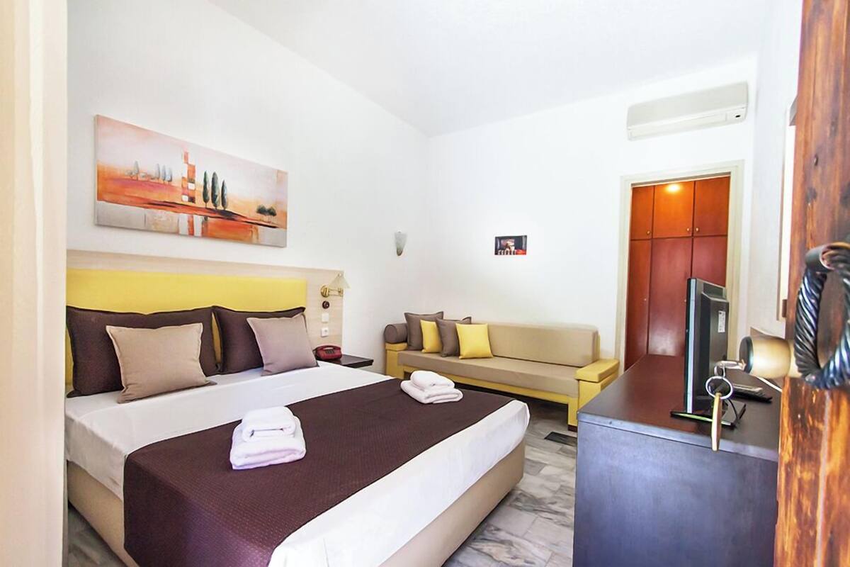 A hotel room with a bed, a sofa, a desk, and a painting on the wall.
