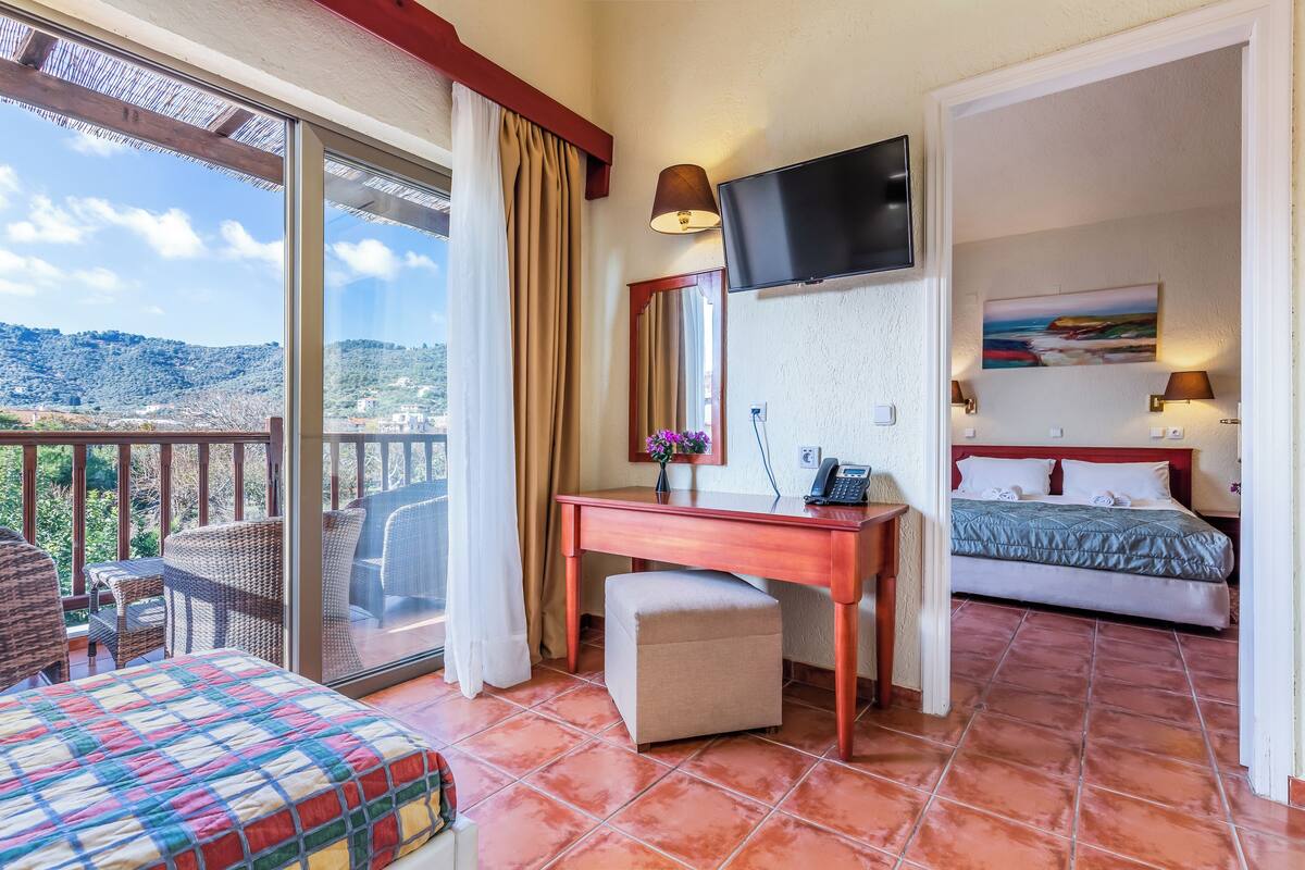 A hotel room with a balcony, a bed, a desk, and a TV.