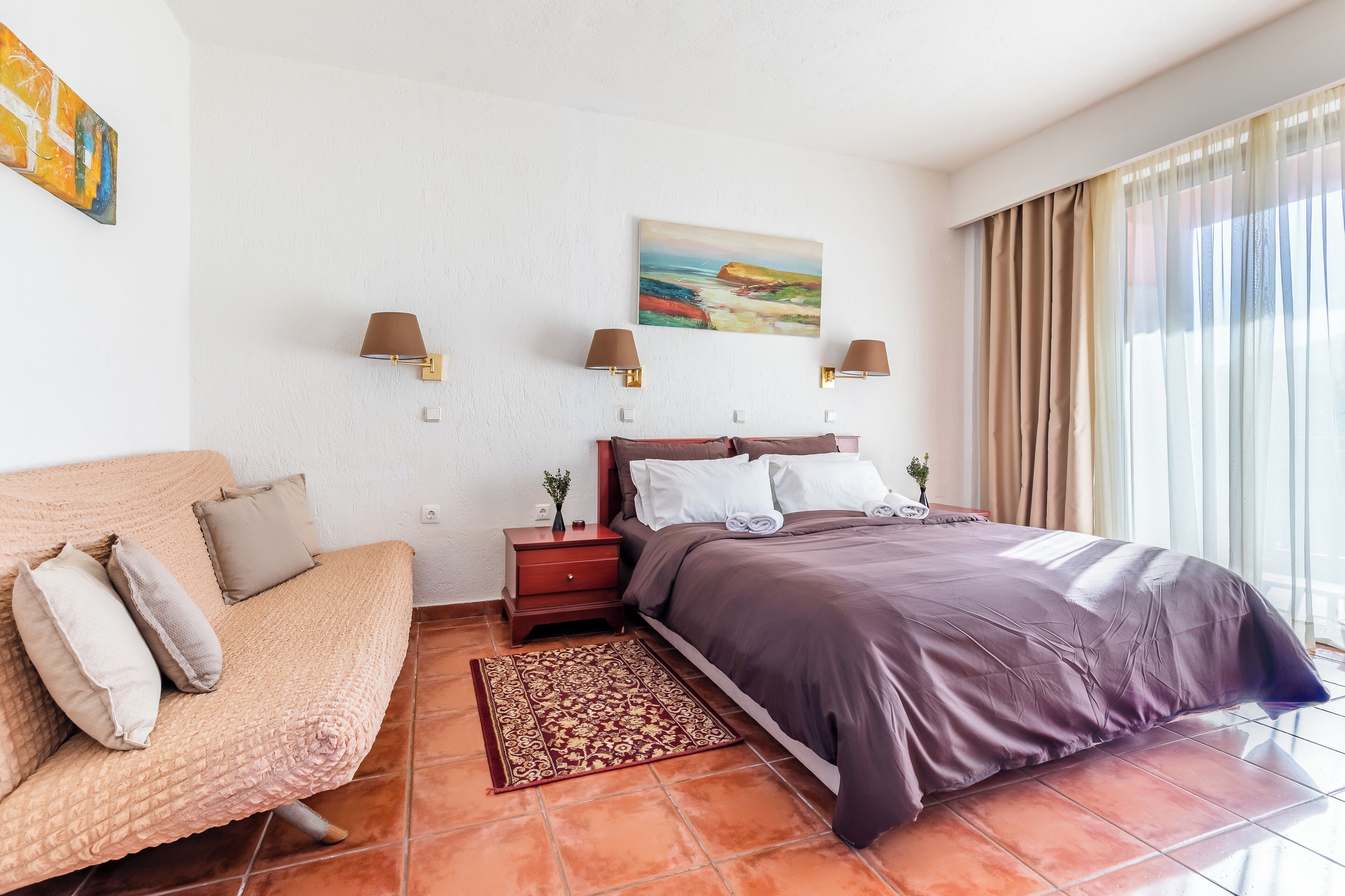 Un dormitorio con cama, sofá, mesita de noche y un cuadro en la pared.