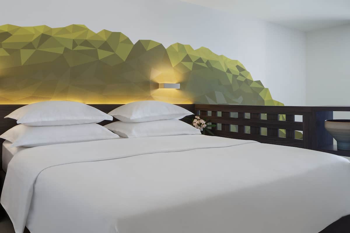 A neatly made bed with white linens, a wooden headboard, and a geometric wall design behind it.