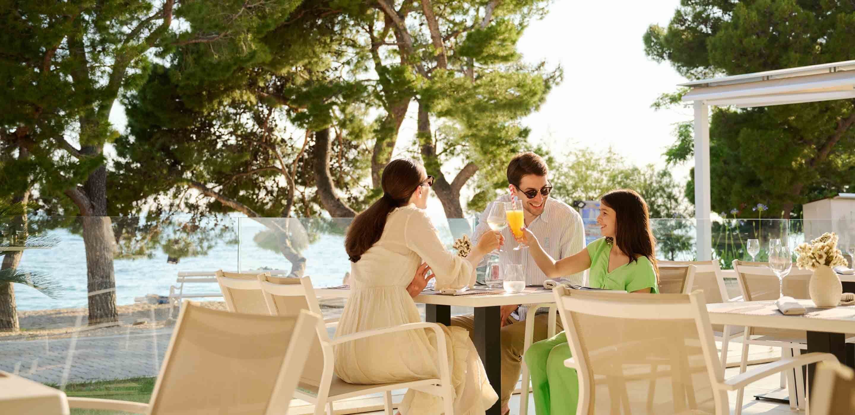 A group of people dining at an outdoor table with a view of the sea.