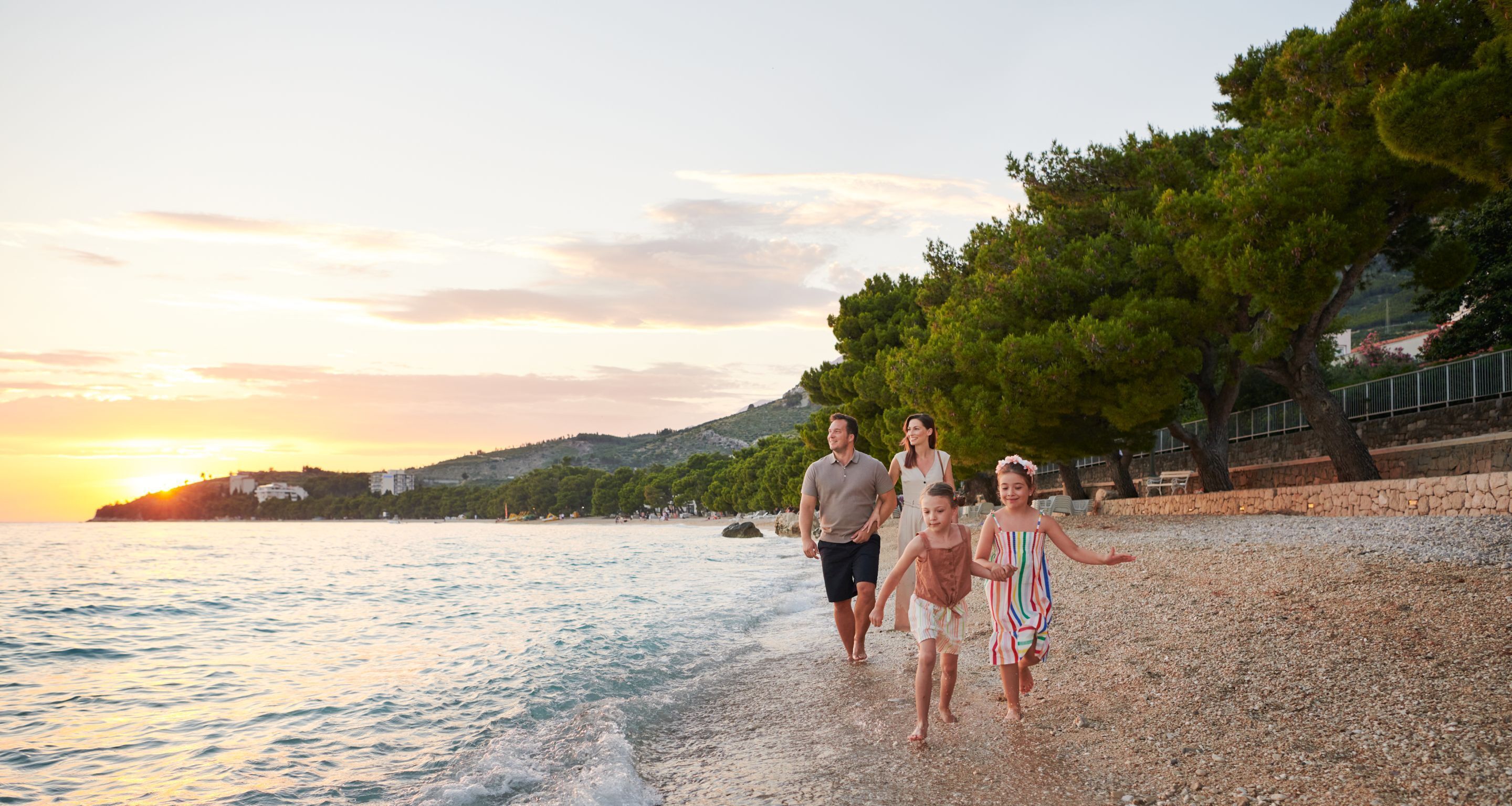 Una familia camina por una playa de guijarros con el sol poniéndose al fondo.