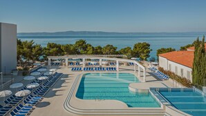 Un área de piscina con sillas de descanso y sombrillas, con vistas a una masa de agua y colinas al lejano.