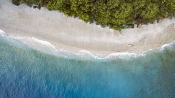 An aerial view of a beach with clear turquoise water and white sand, bordered by dense green foliage.