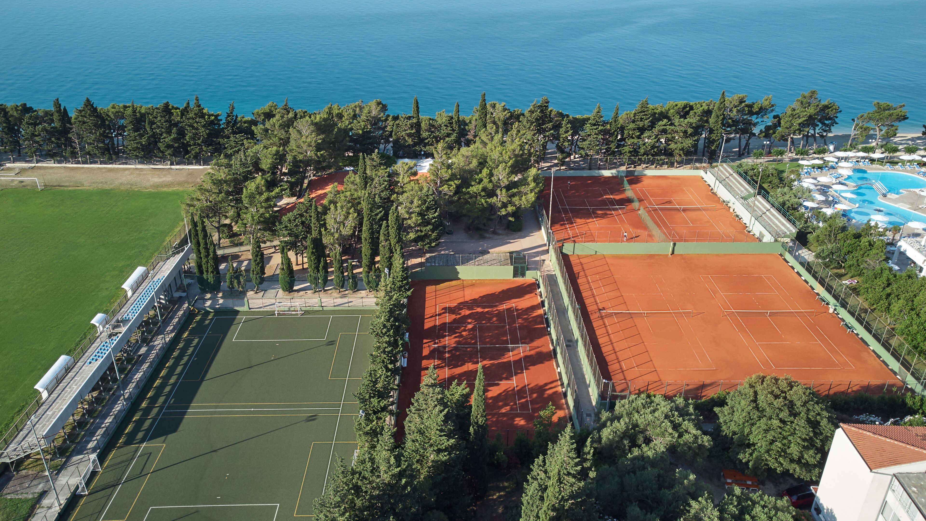 An aerial view of a sports complex with tennis courts, a swimming pool, and a green field.