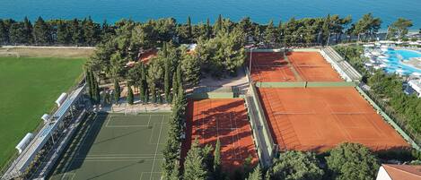 An aerial view of a sports complex with tennis courts, a swimming pool, and a green field.