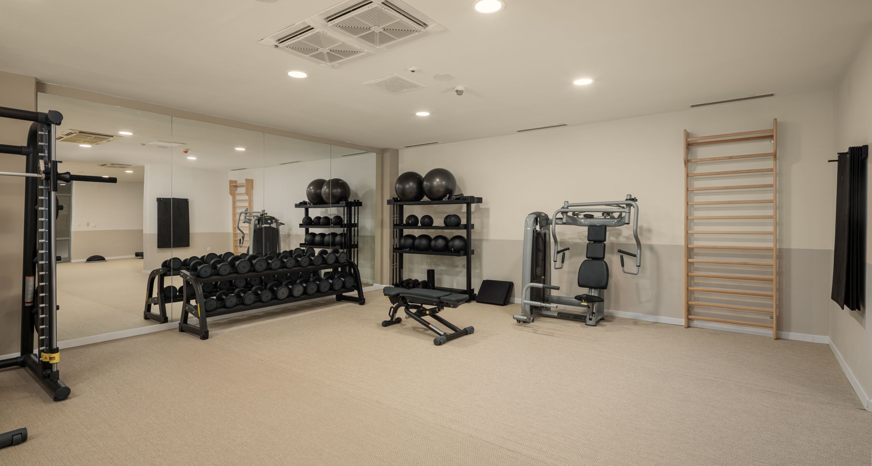 Ein Fitnessraum mit Trainingsgeräten, einer Hantelbank und einem Spiegel.