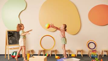 Una habitación con una pizarra, taburetes de madera y una pelota colorida.