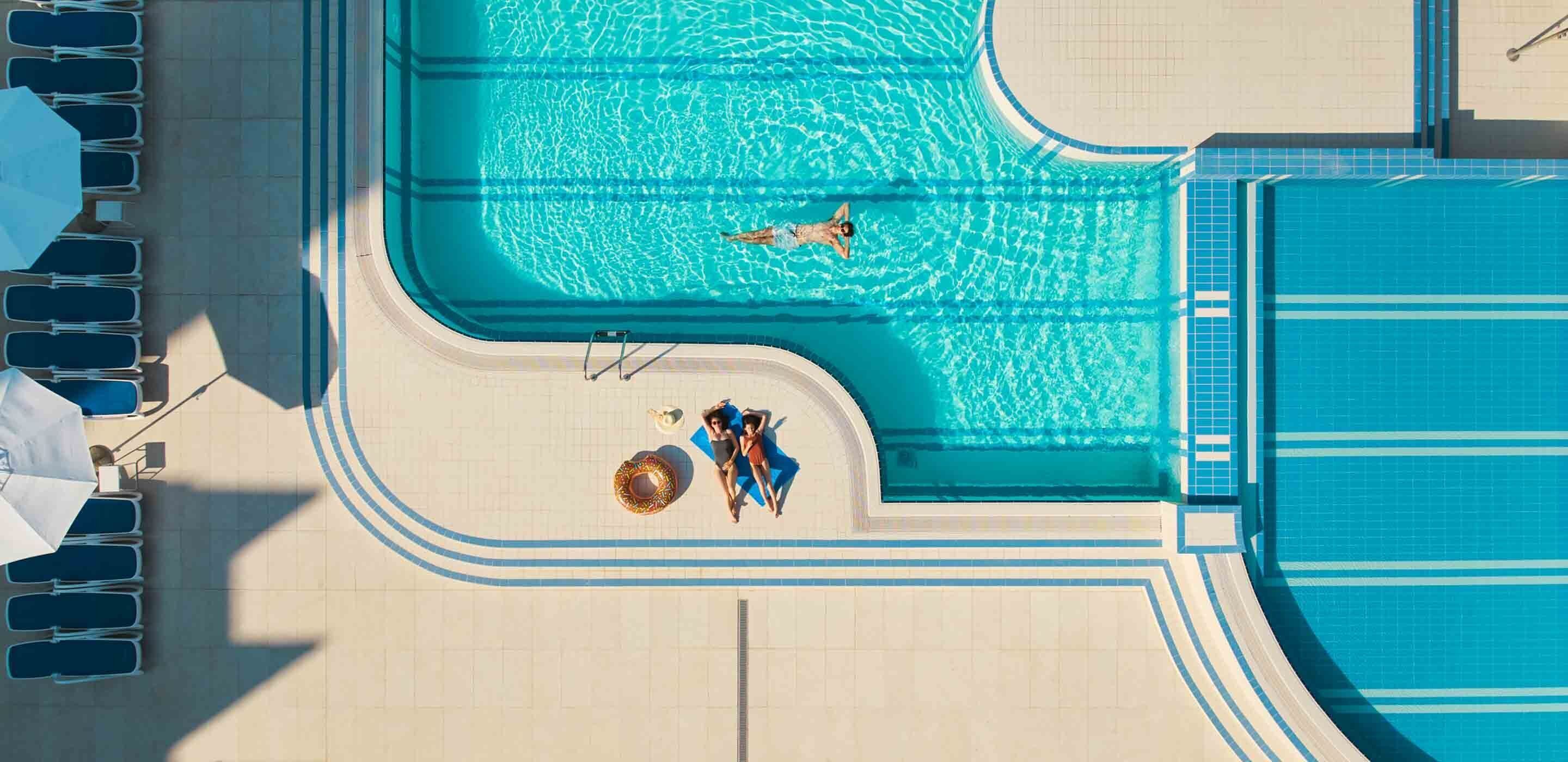 Piscina com deck revestido, cadeiras de sol e toldo.