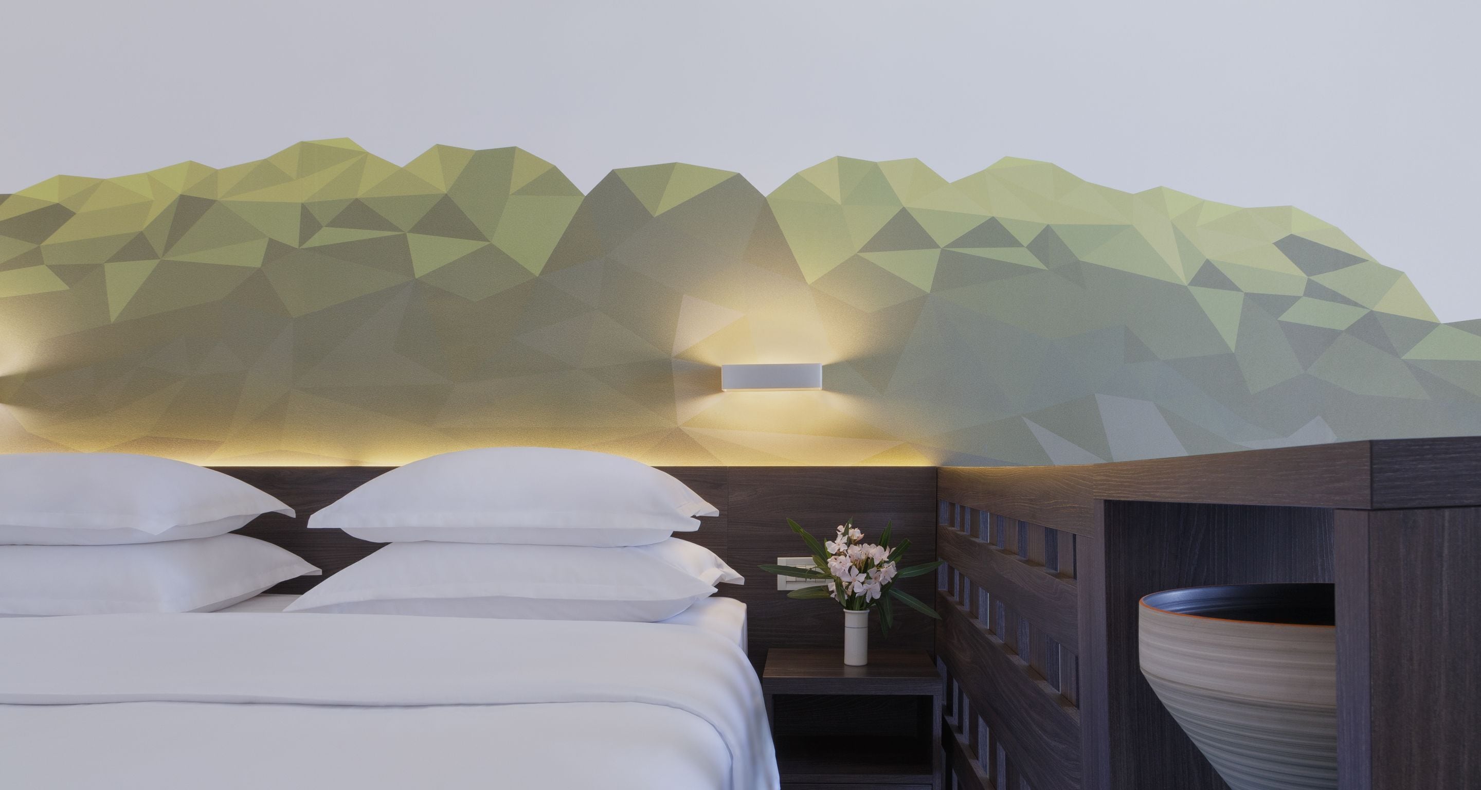 Ein modernes Hotelzimmer mit Wandgestaltung im Bergmotiv, ein ordentlich bezogenes Bett mit weißer Bettwäsche, ein Nachttisch mit Blumenvase und eine große Vase auf dem Nachttisch.