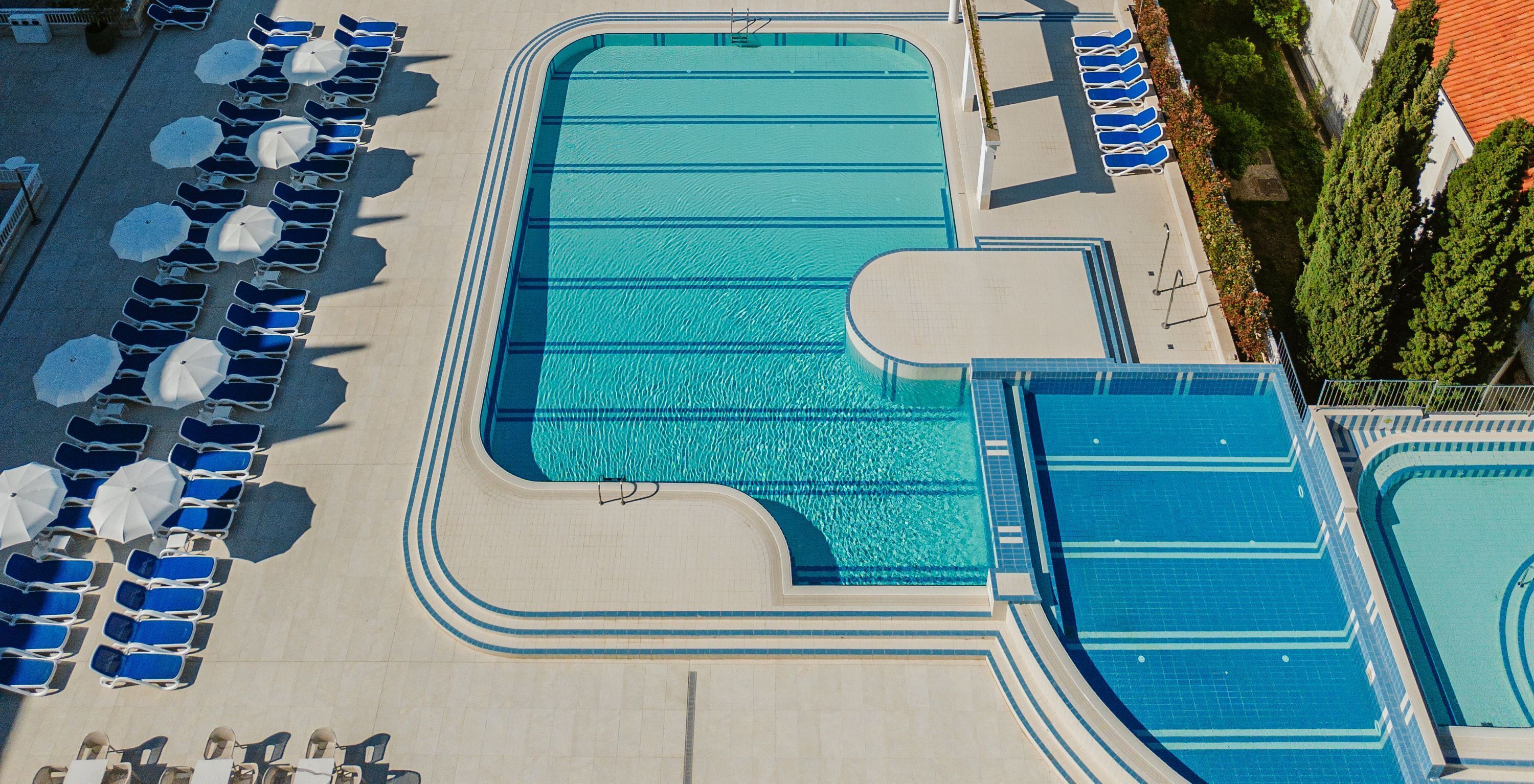 A large outdoor swimming pool with multiple lanes, surrounded by lounge chairs and umbrellas.