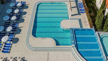 A large outdoor swimming pool with multiple lanes, surrounded by lounge chairs and umbrellas.