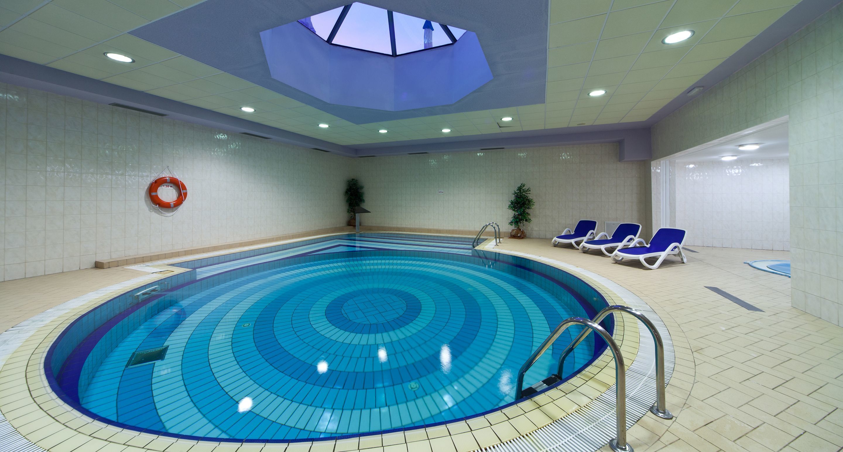 Una piscina interior con tragaluces, paredes de azulejos y sillones de descanso.