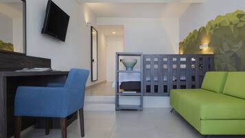A modern living room with a green sofa, a blue chair, a wooden desk, and a TV mounted on the wall.
