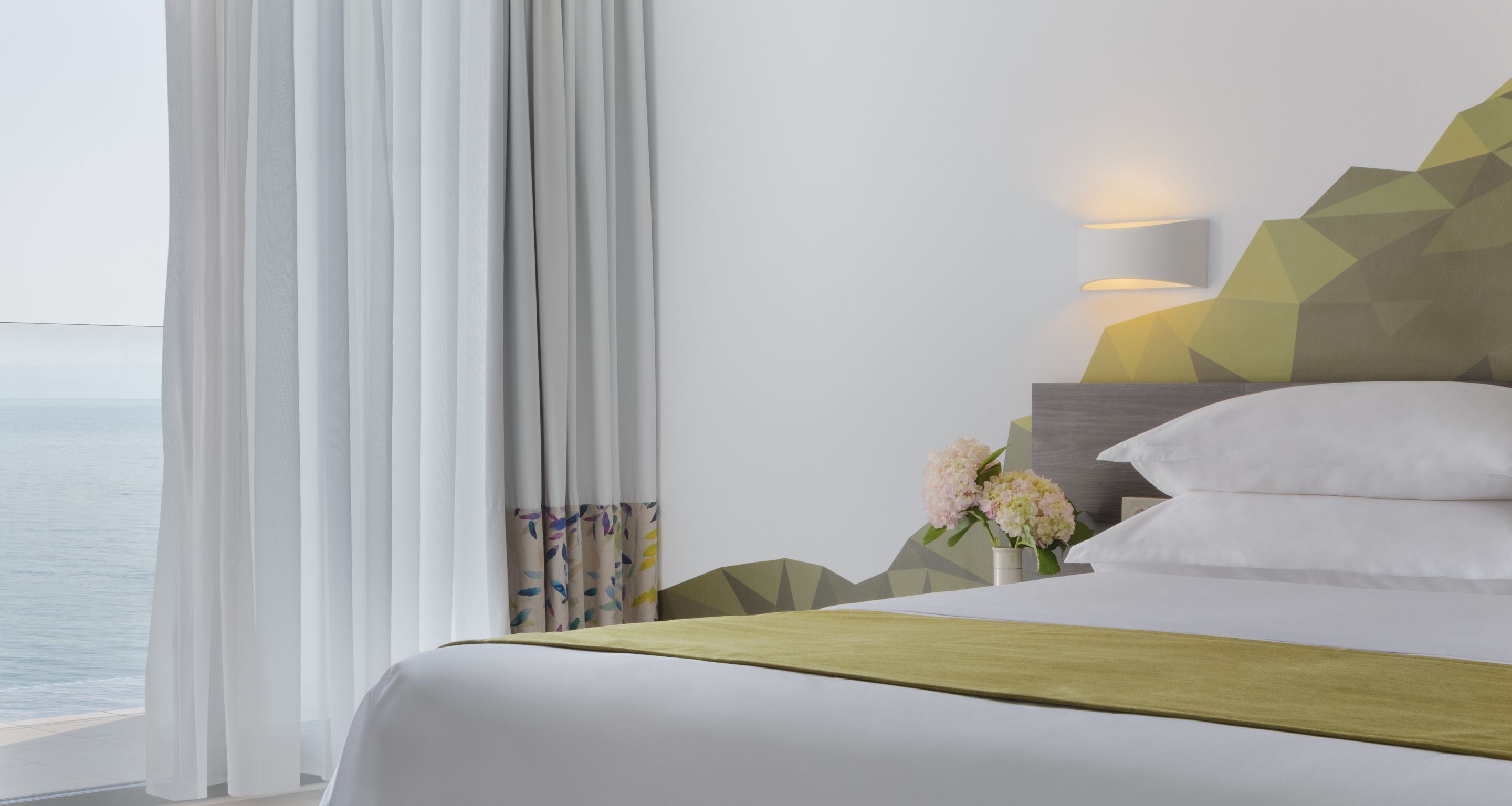 Una habitación de hotel con cama, mesita de noche, lámpara y vista al mar.