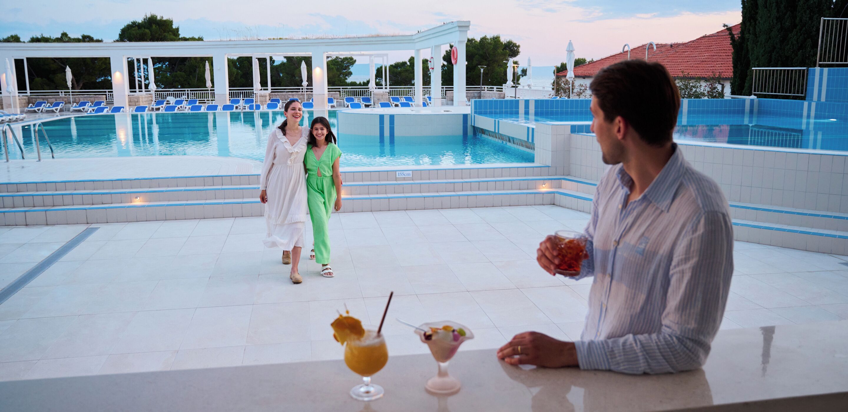 Zona de piscina con sillones de descanso y un bar con bebidas.