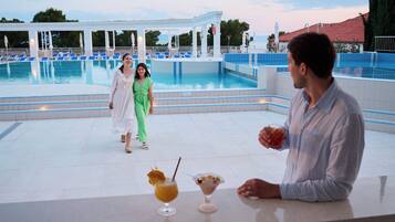 Zona de piscina con sillones de descanso y un bar con bebidas.