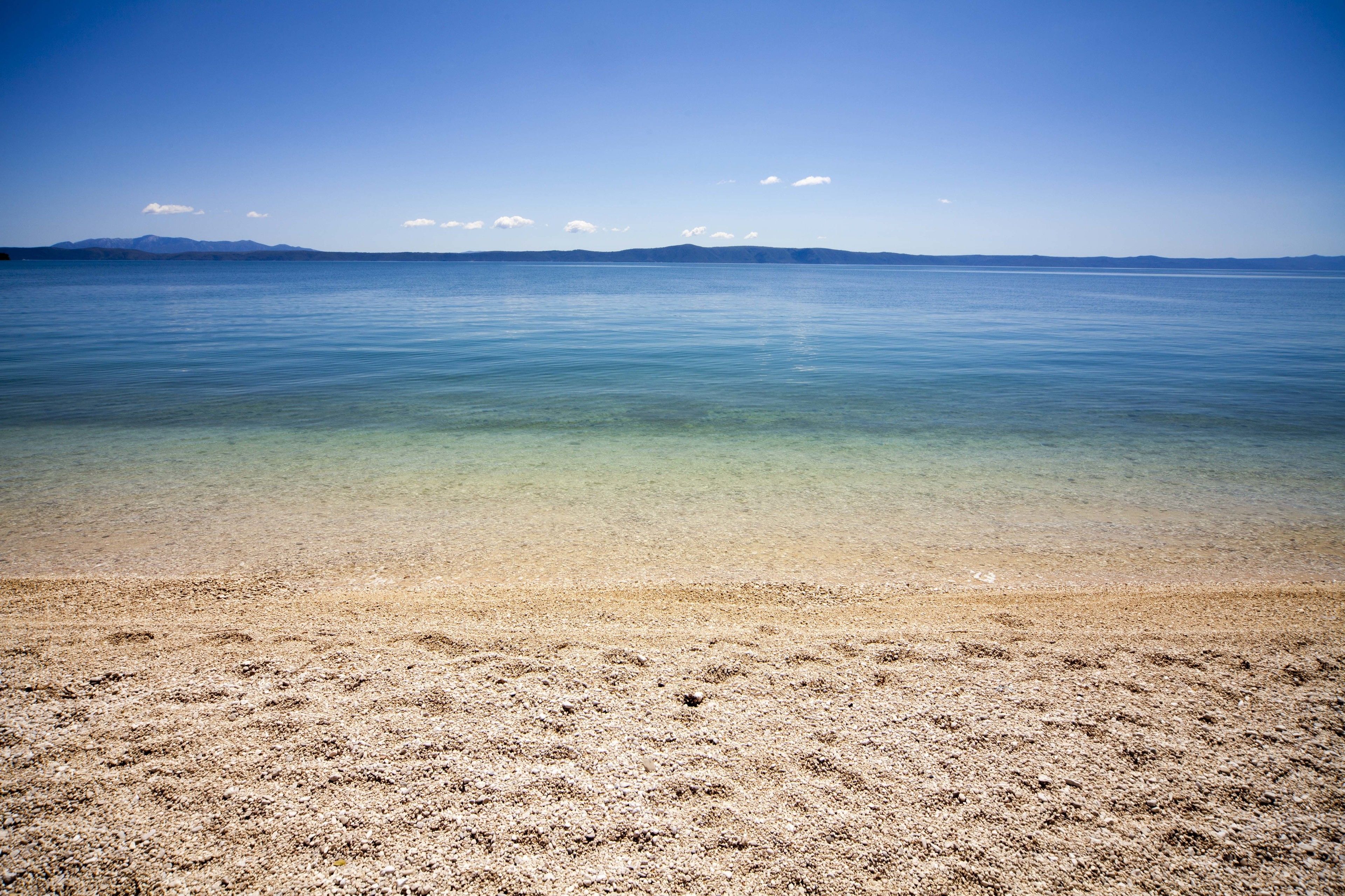 Una playa con agua cristalina y una cadena montañosa al fondo.