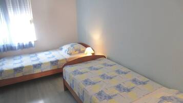 A room with two single beds, a window with curtains, and a bedside lamp.