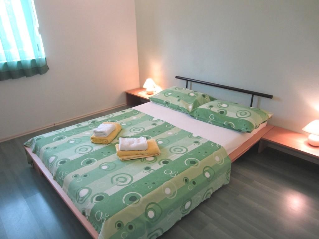 A single bed with a green patterned bedspread and pillows, two bedside lamps, and a nightstand with a lamp.