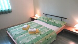 Ein Einzelbett mit einem grün gemusterten Überwurf und Kissen, zwei Nachttischlampen und ein Nachttisch mit einer Lampe.