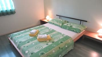 A single bed with a green patterned bedspread and pillows, two bedside lamps, and a nightstand with a lamp.