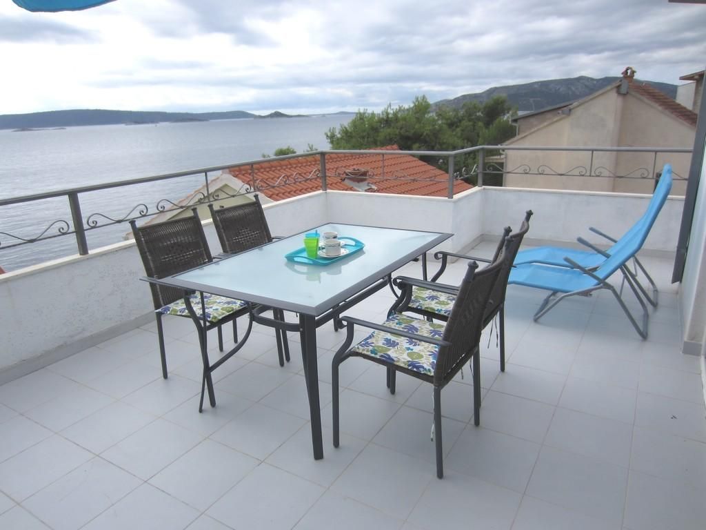 A balcony with a table and chairs, overlooking a body of water and hills.