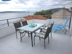 A balcony with a table and chairs, overlooking a body of water and hills. - Apartmani Kelam (Okrug)