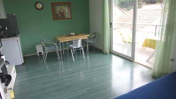 A room with a dining table and chairs, a kitchenette, and a sliding glass door to the outside.