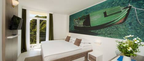 Une chambre d’hôtel moderne avec un grand lit, un téléviseur à écran plat, un tableau représentant un bateau et un bureau agrémenté d’un vase de fleurs.