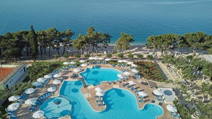 An aerial view of a resort with a large swimming pool, sun loungers, and a beach area. - Bluesun Hotel Neptun (Tucepi)