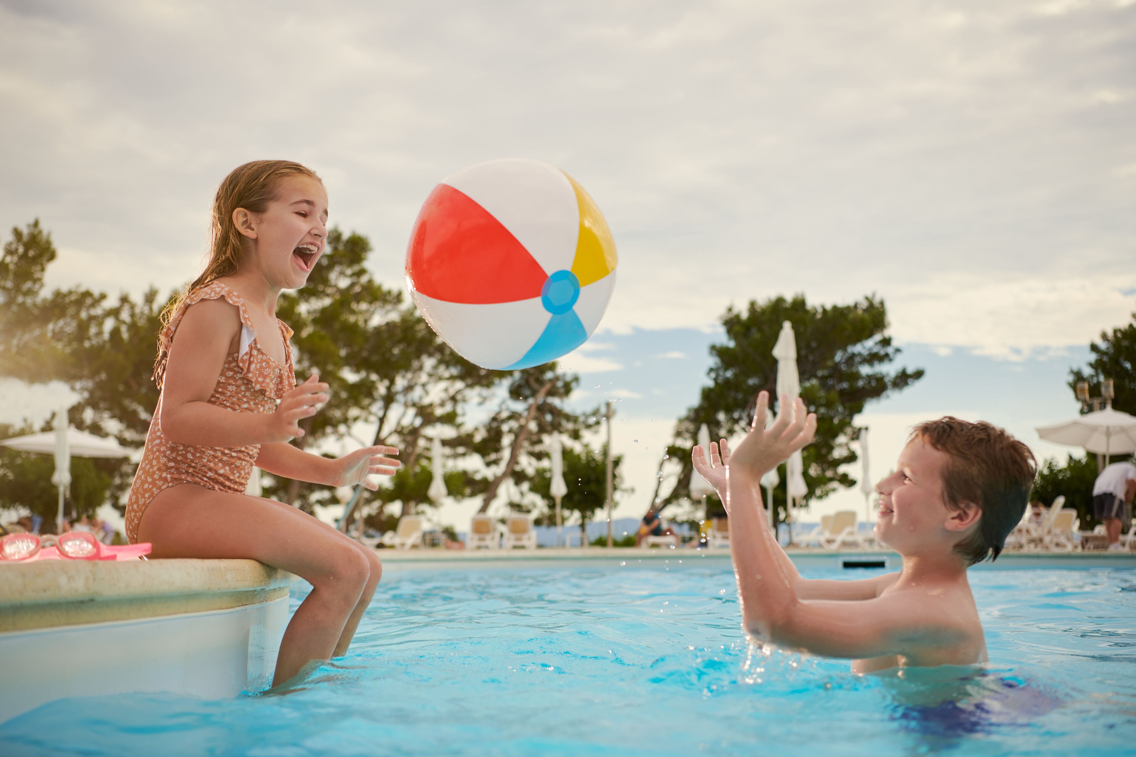 Szenenbild am Pool: eine Person sitzt am Beckenrand, eine andere befindet sich im Wasser.