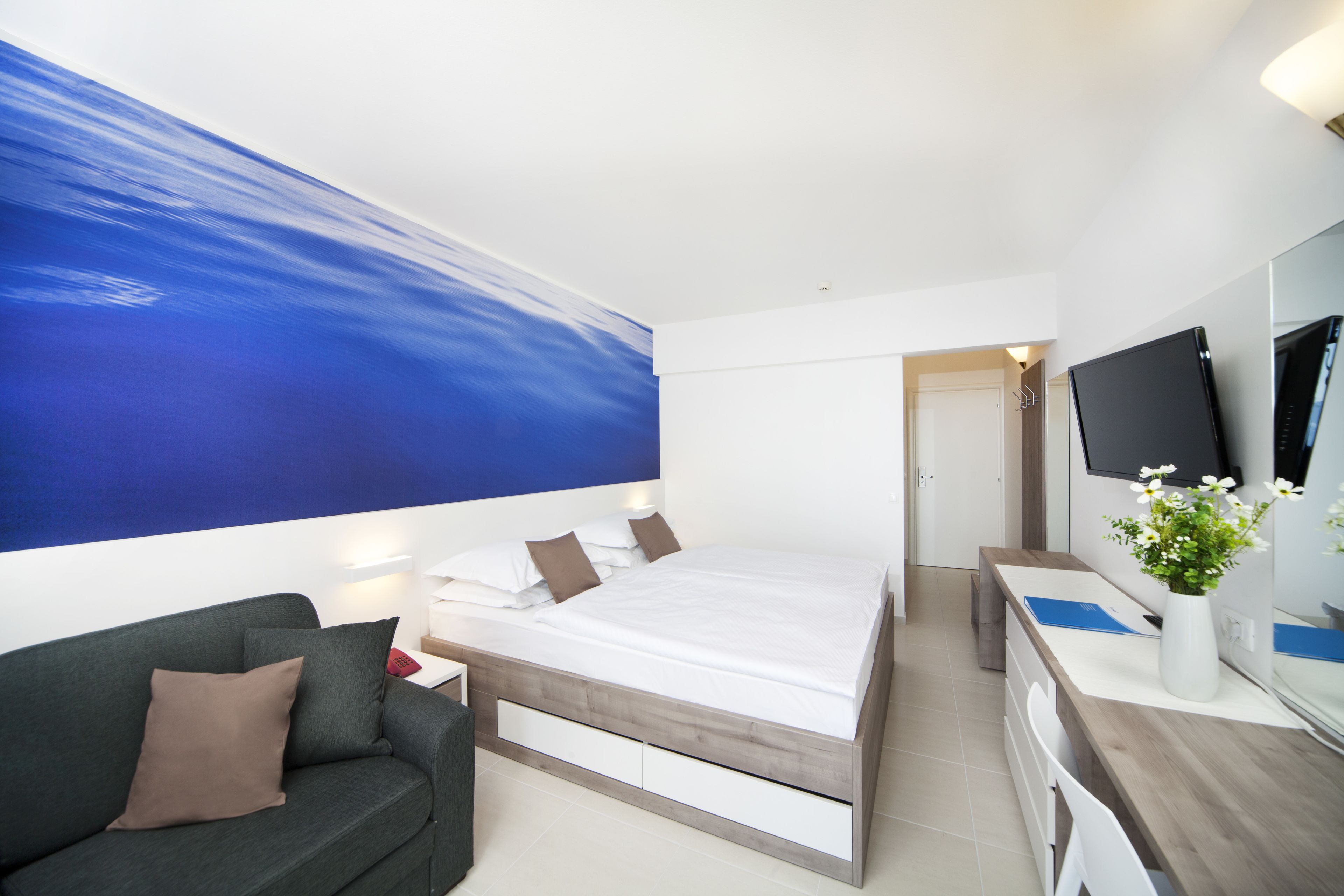 Una habitación de hotel moderna con una cama grande, un sofá, un escritorio con una computadora y un televisor.