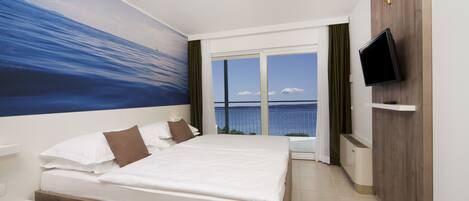 Een hotelkamer met een groot bed, een aan de muur bevestigde televisie en uitzicht op zee.