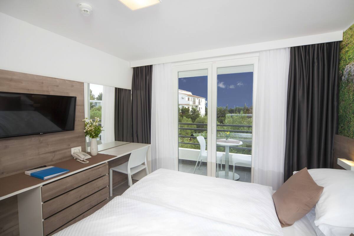 A modern hotel room with a bed, a desk, a flat-screen TV, a phone, and a view of the outdoors.
