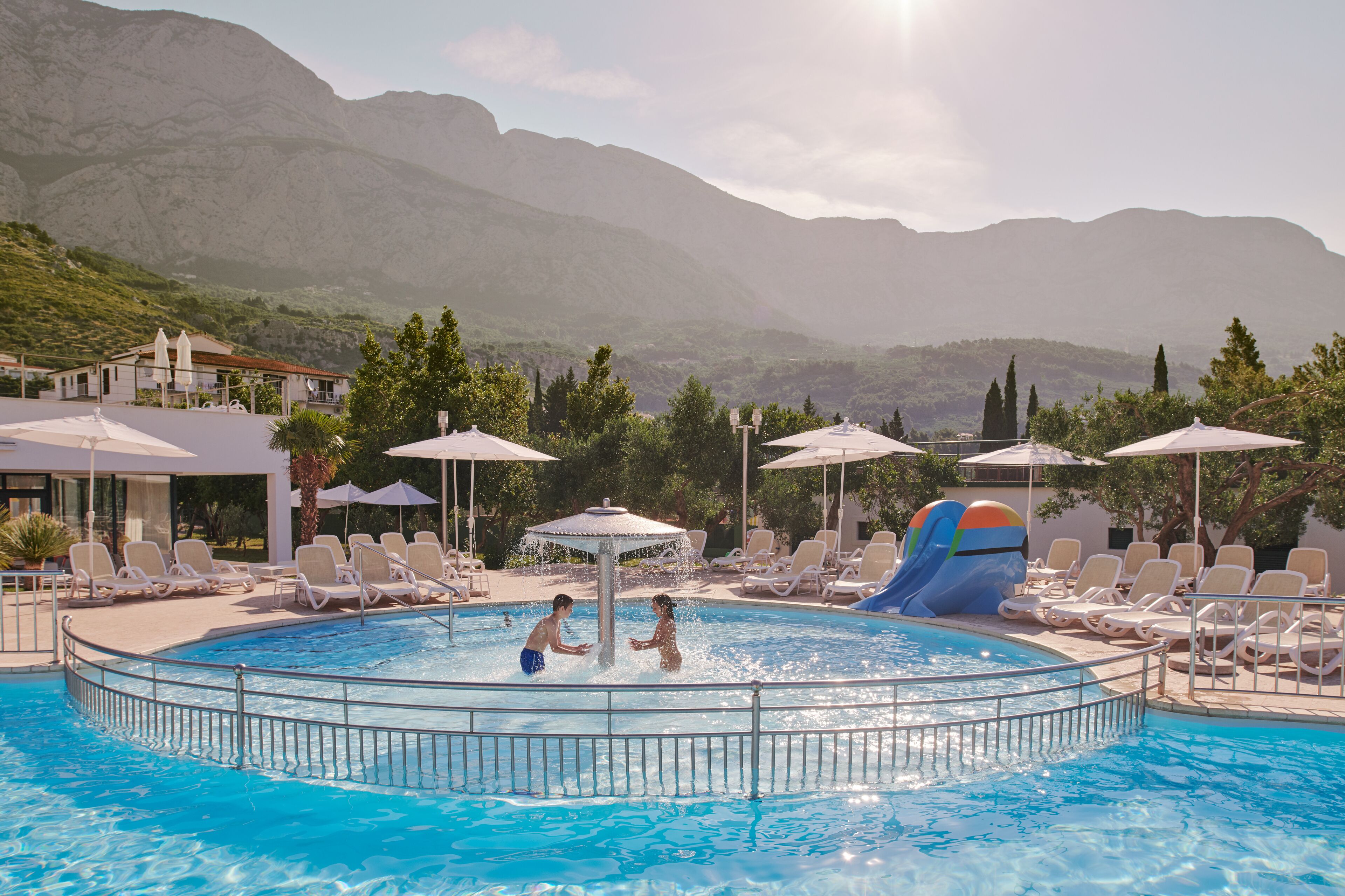 A pool area with lounge chairs, umbrellas, and a water slide.