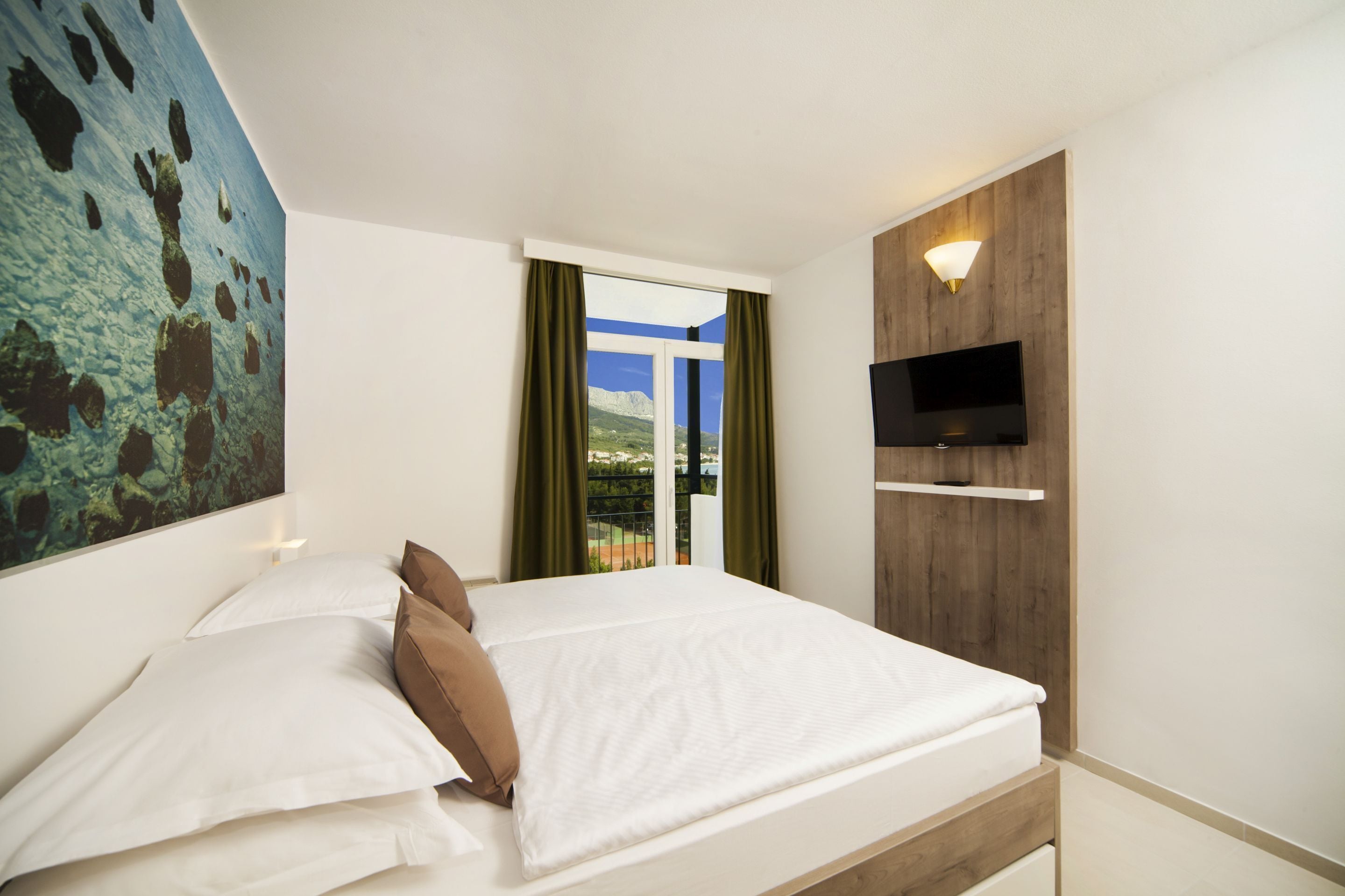 Une chambre à coucher avec un lit, un téléviseur fixé au mur et une fenêtre avec des rideaux.