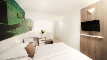 A modern hotel room with a large bed, a desk with a chair, a flat-screen TV mounted on a wooden wall, and a large painting of a boat on the wall.
