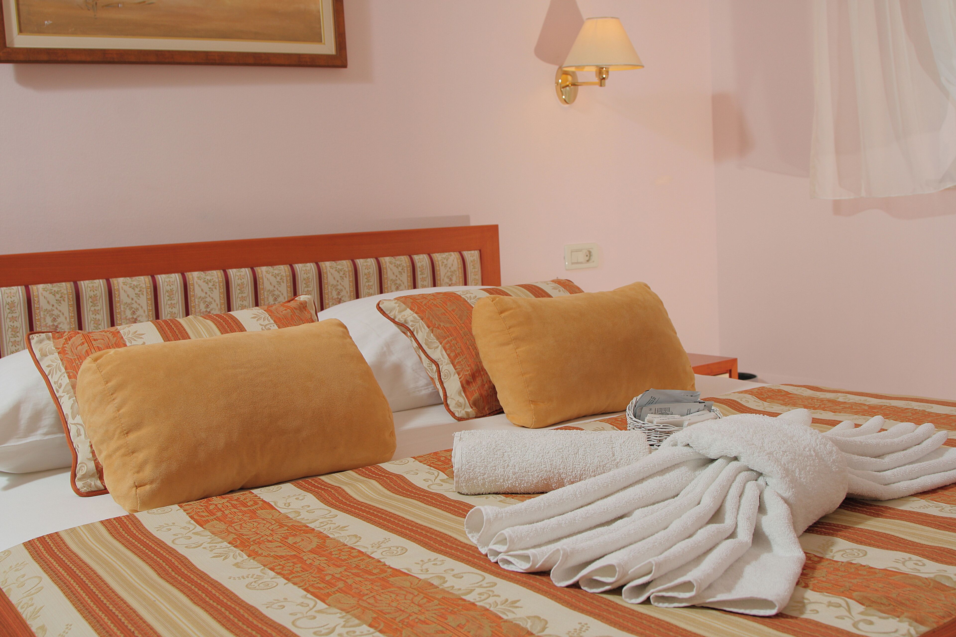 Une chambre d’hôtel avec un lit, des oreillers, une lampe et une serviette pliée.