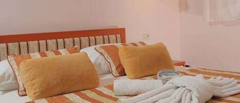Une chambre d’hôtel avec un lit, des oreillers, une lampe et une serviette pliée.