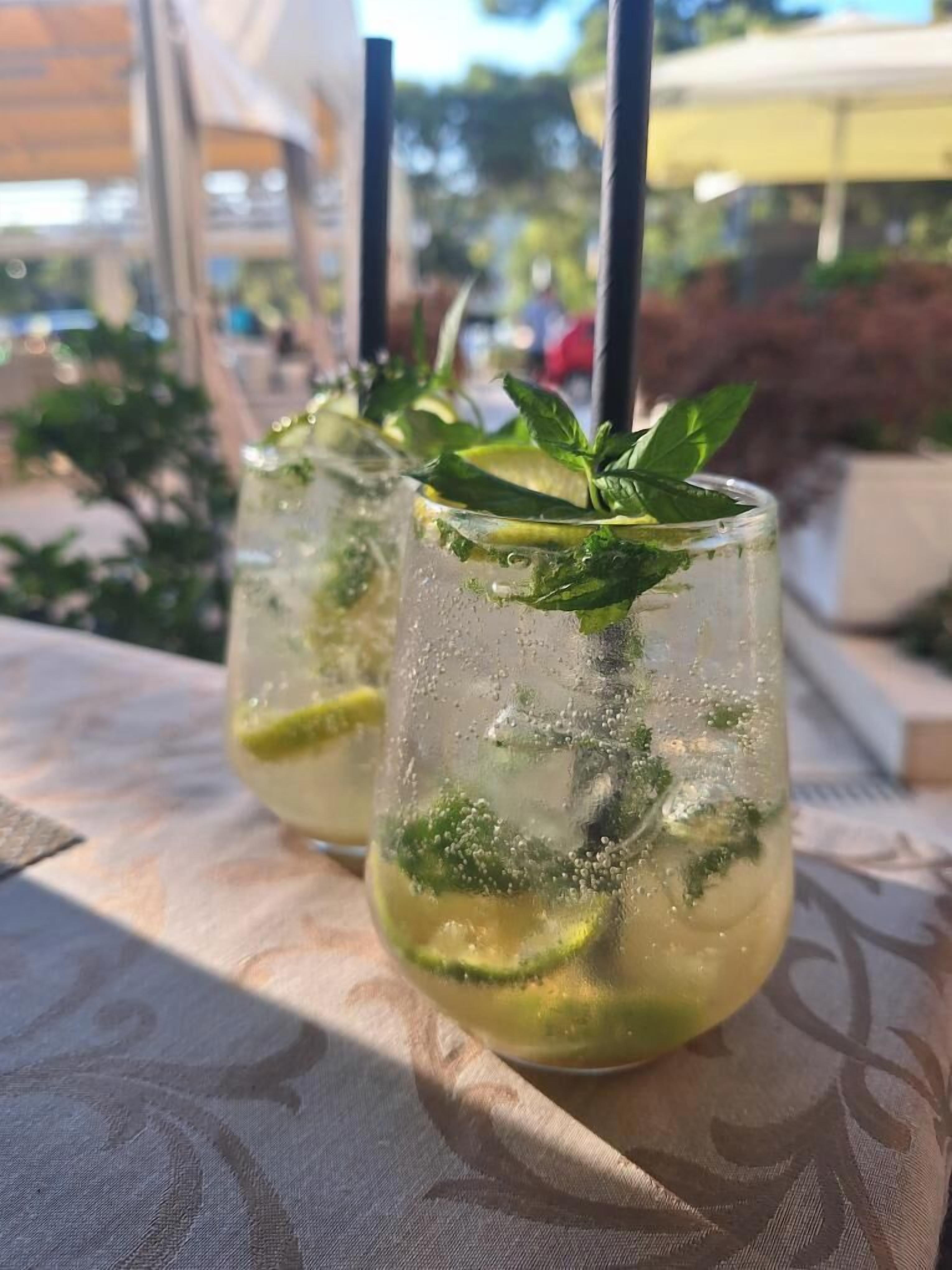 Two glasses of a beverage with mint leaves, placed on a table with a patterned tablecloth.
